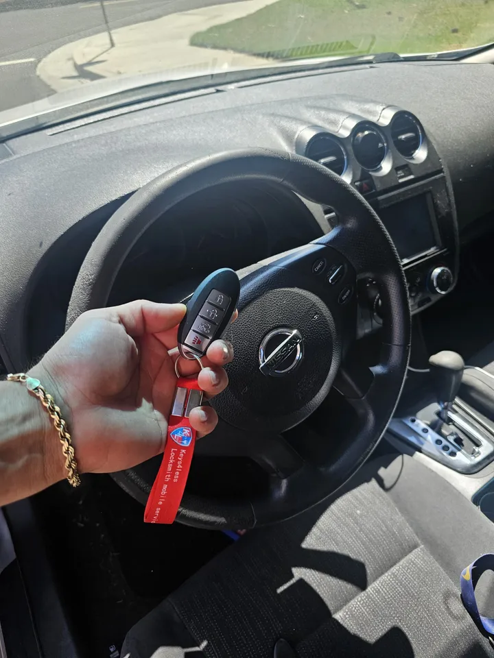 Nissan smart key held in front of the Altima steering wheel.