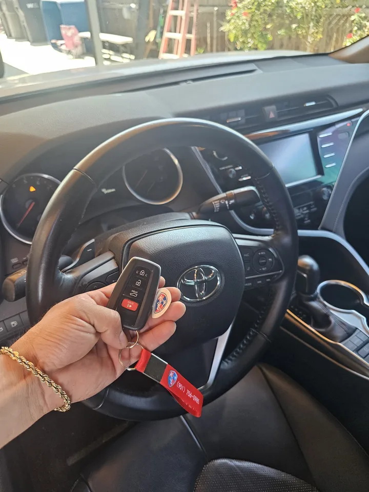 Toyota smart key held in front of the Camry steering wheel.